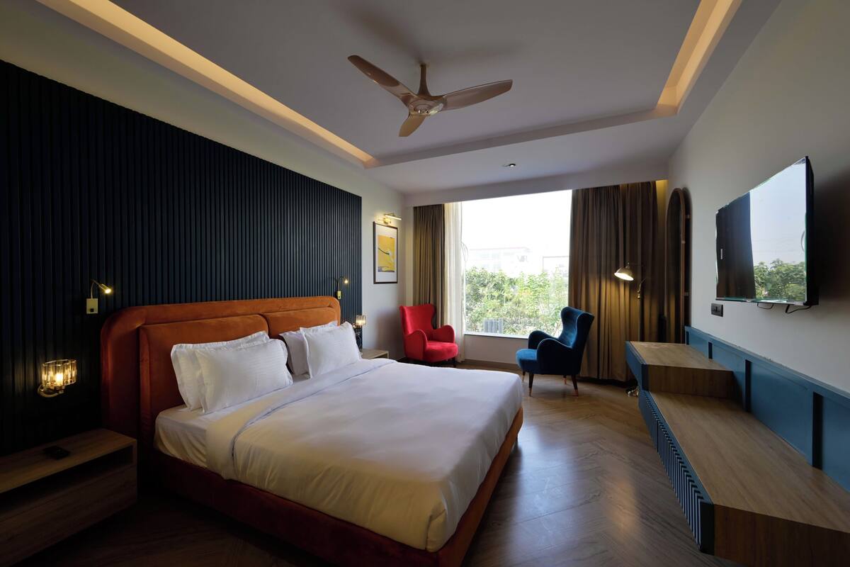 A hotel room with a large bed, a desk, a chair, a ceiling fan, and a TV mounted on the wall.