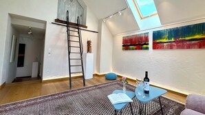 Amplia sala de estar con un altillo con cama, tragaluces, colección de arte moderno y una zona de estar acogedora con un libro y vino.