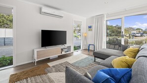 Uma sala de estar moderna com televisão de tela plana, sofá e uma grande janela com vista para o exterior.