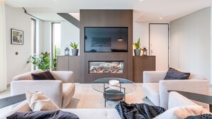 A modern living room with a fireplace, comfortable seating, and a flat-screen TV mounted above it. - Villa Memorias | Modern | 3 Bedrooms | Albufeira (Albufeira)