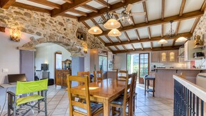 A spacious kitchen with stone walls, wooden beams, and a large dining table with chairs.