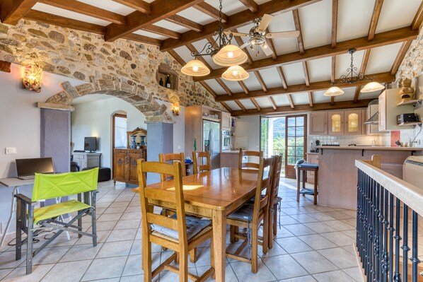 Une cuisine spacieuse avec des murs en pierre, des poutres en bois et une grande table à manger entourée de chaises.