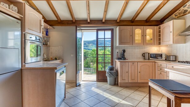 A kitchen with wooden beams, a refrigerator, oven, microwave, and a view of greenery through the door.