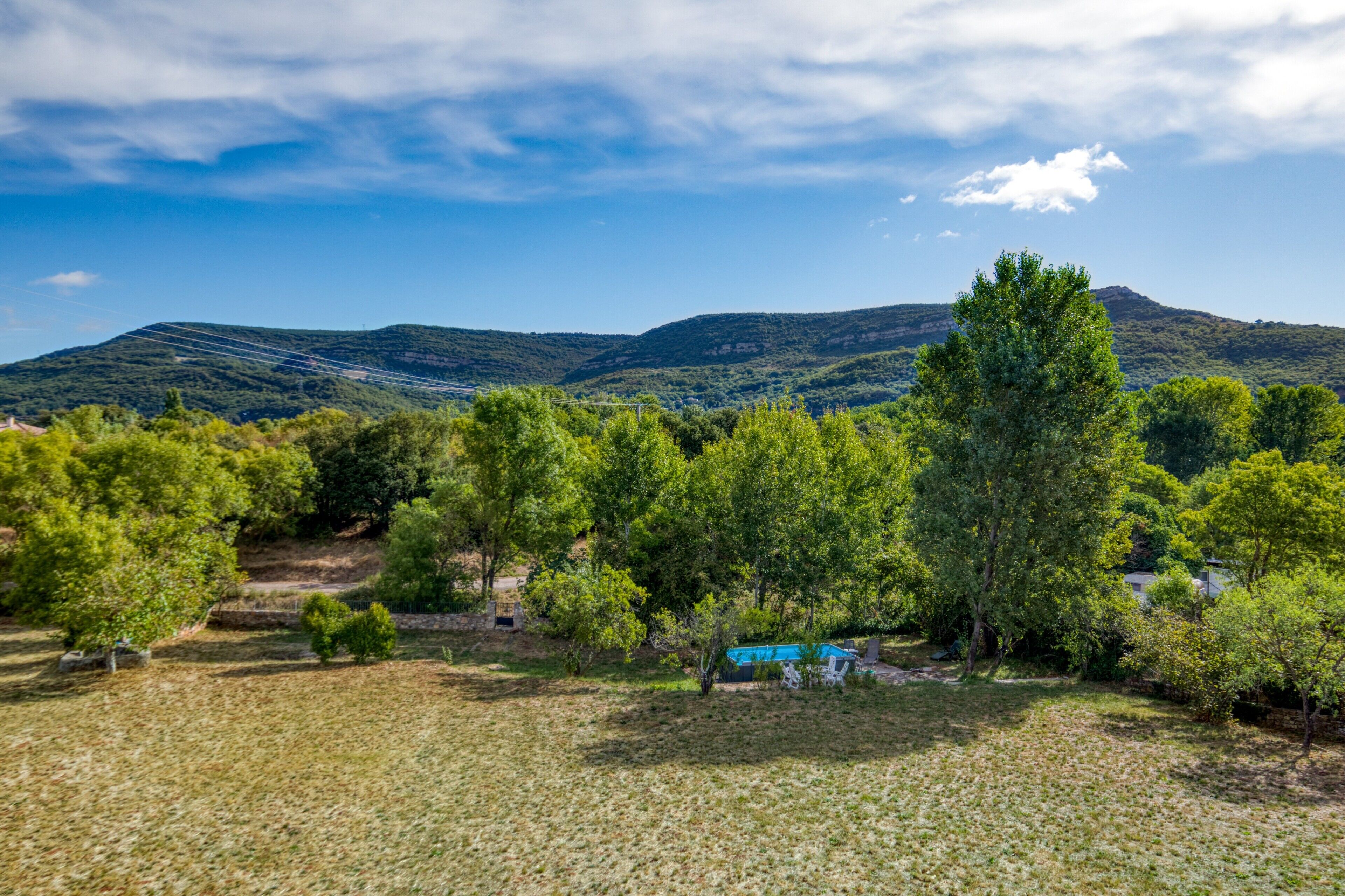 Ländliche Landschaft mit Bäumen, einem kleinen Gebäude und Hügeln im Hintergrund.