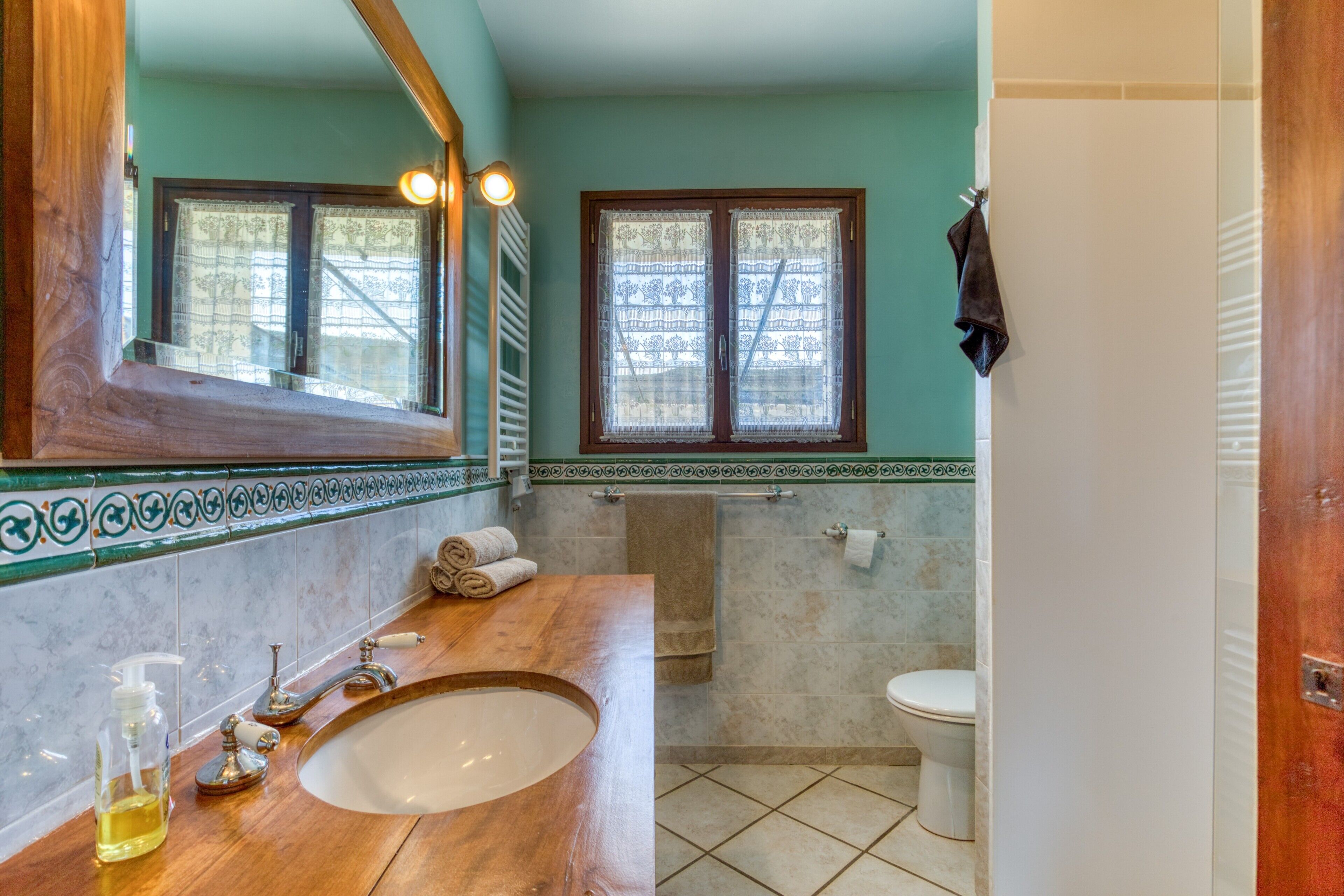 A bathroom with a wooden vanity, a large mirror, a window, and a toilet.