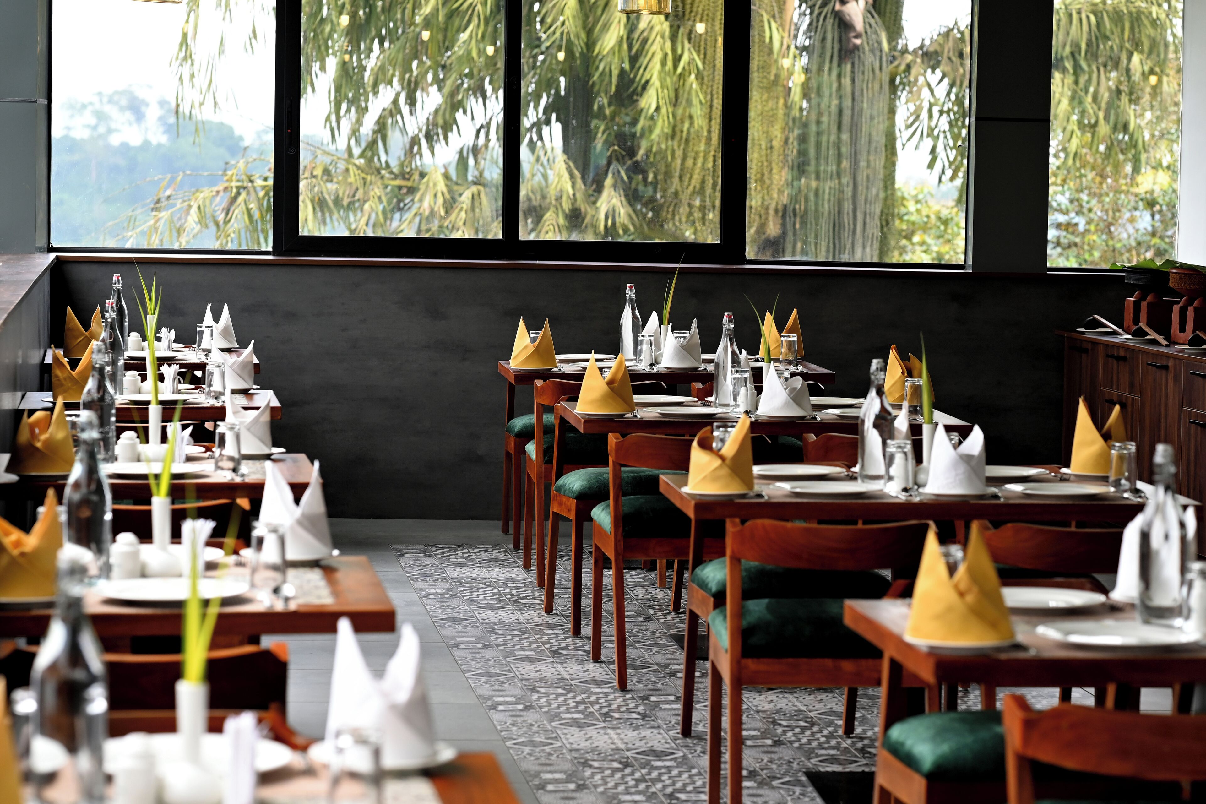 A restaurant with tables set for dining, chairs, and a view of palm trees through large windows.