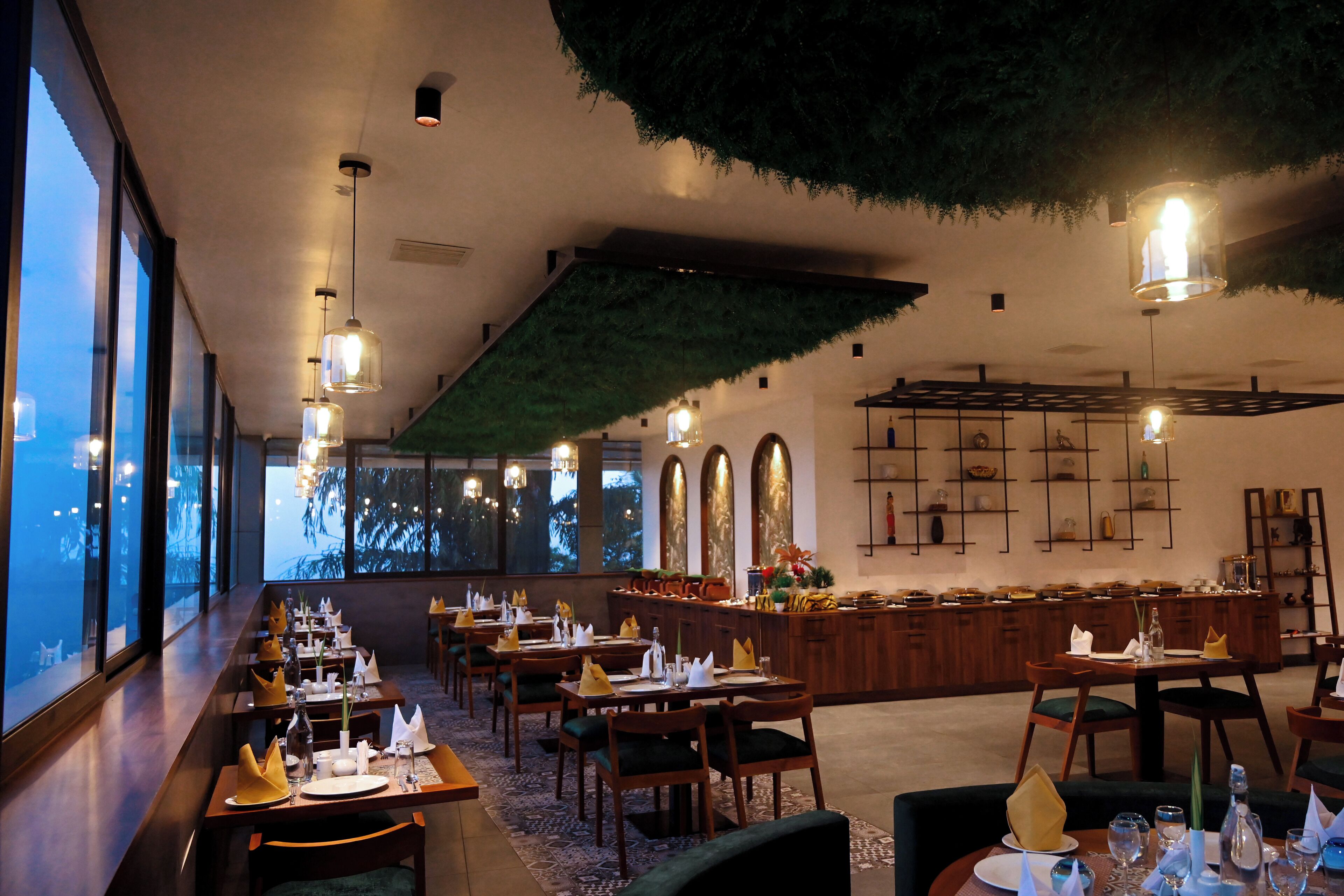 A restaurant with long tables, wooden chairs, and hanging pendant lights.
