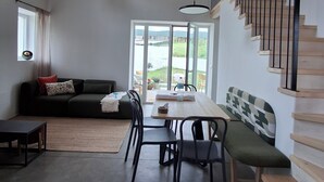 Ein stilvolles Wohnzimmer mit Holzbalkendecke, einem Essbereich mit Tisch und Stühlen, einer Couch und einer Treppe mit Geländer.