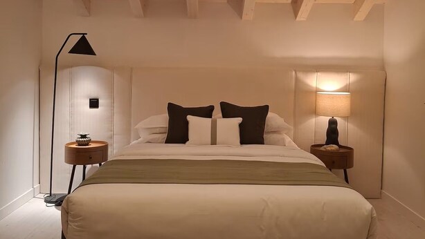 Ein Schlafzimmer mit Oberlicht, einem Bett, zwei Nachttischen mit Lampen und einem gemusterten Teppich.