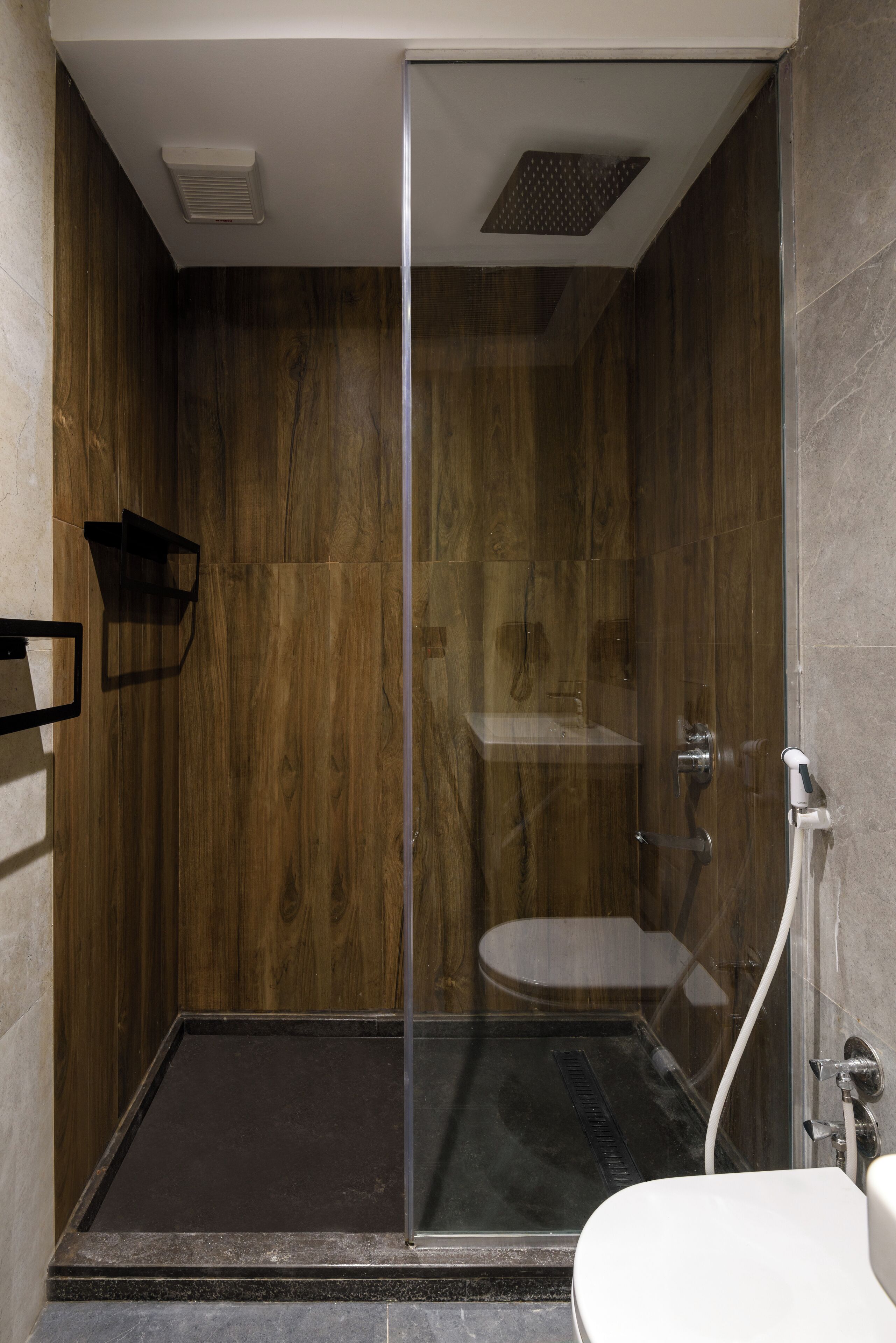 Un baño moderno con ducha de vidrio, pared de madera y lavamanos blanco.