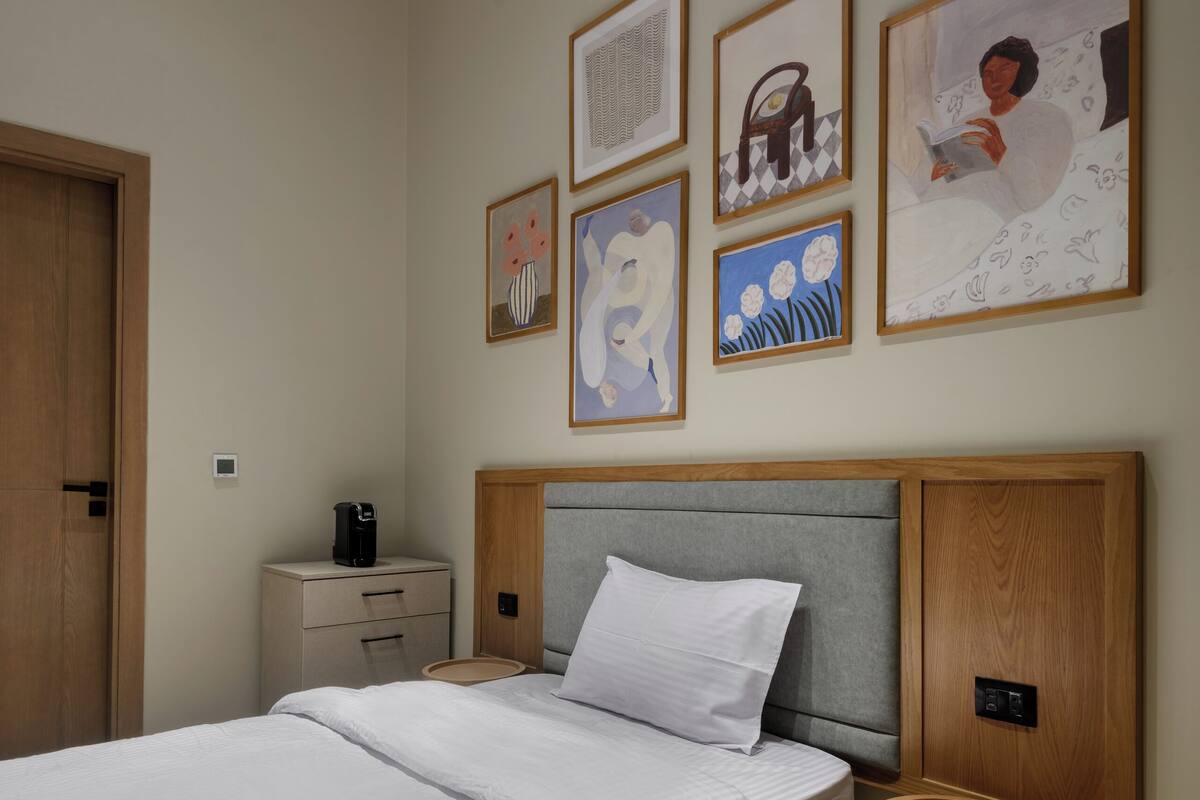 A neatly arranged bedroom with a large bed, a bedside table, a round side table, and several framed artworks on the wall.