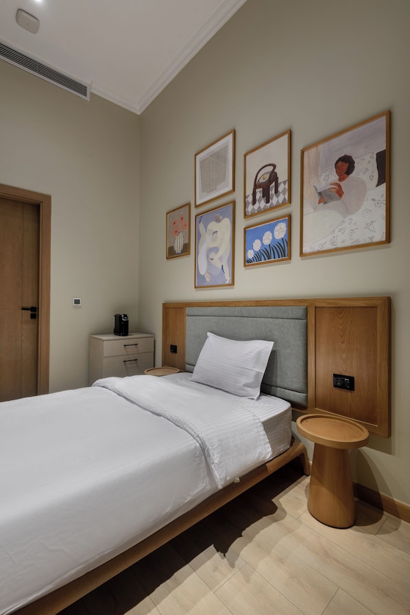 A neatly arranged bedroom with a large bed, a bedside table, a round side table, and several framed artworks on the wall. - Hazel Spaces DownTown (Cairo)