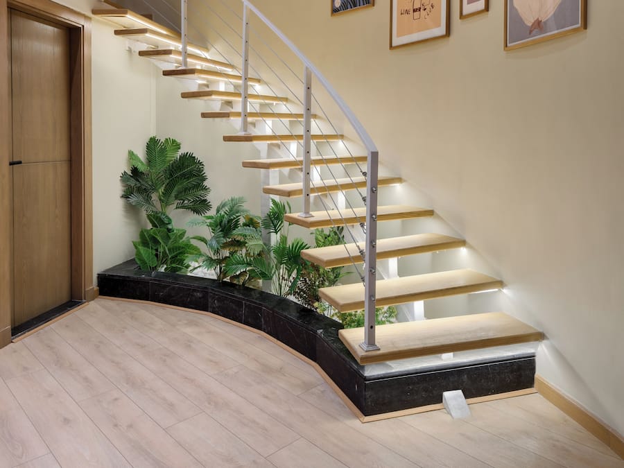 Una escalera moderna con detalles de madera y barandillas de vidrio, rodeada de diversas obras de arte enmarcadas en las paredes.