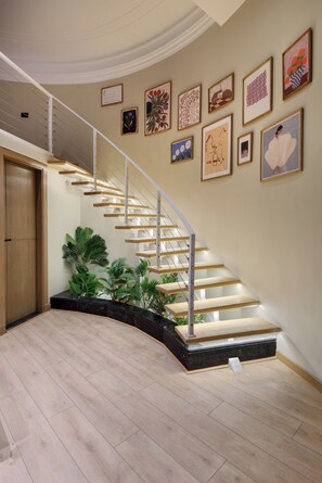 A modern staircase with a wooden finish and glass railings, surrounded by various framed artworks on the walls. - Hazel Spaces DownTown (Cairo)