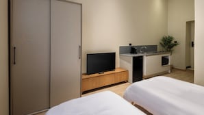 A modern hotel room with a large wardrobe, a flat-screen TV on a wooden console, a small kitchenette, and two beds. - Hazel Spaces DownTown (Cairo)