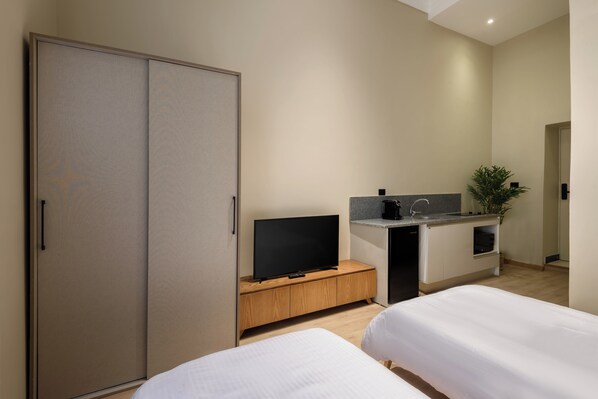A modern hotel room with a large wardrobe, a flat-screen TV on a wooden console, a small kitchenette, and two beds. - Hazel Spaces DownTown (Cairo)