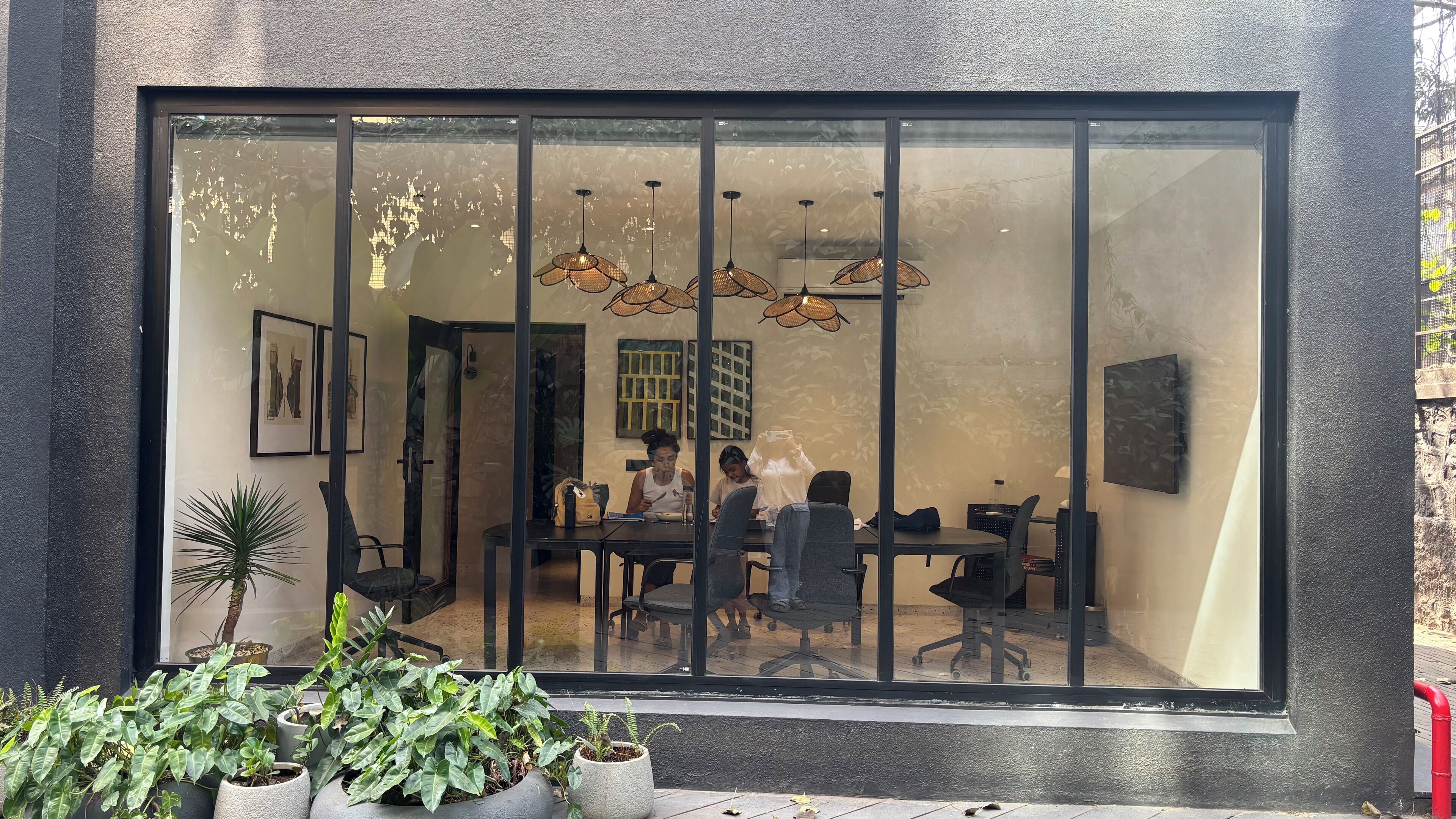 A modern interior with a large glass window, office chairs, a table, and hanging pendant lights.
