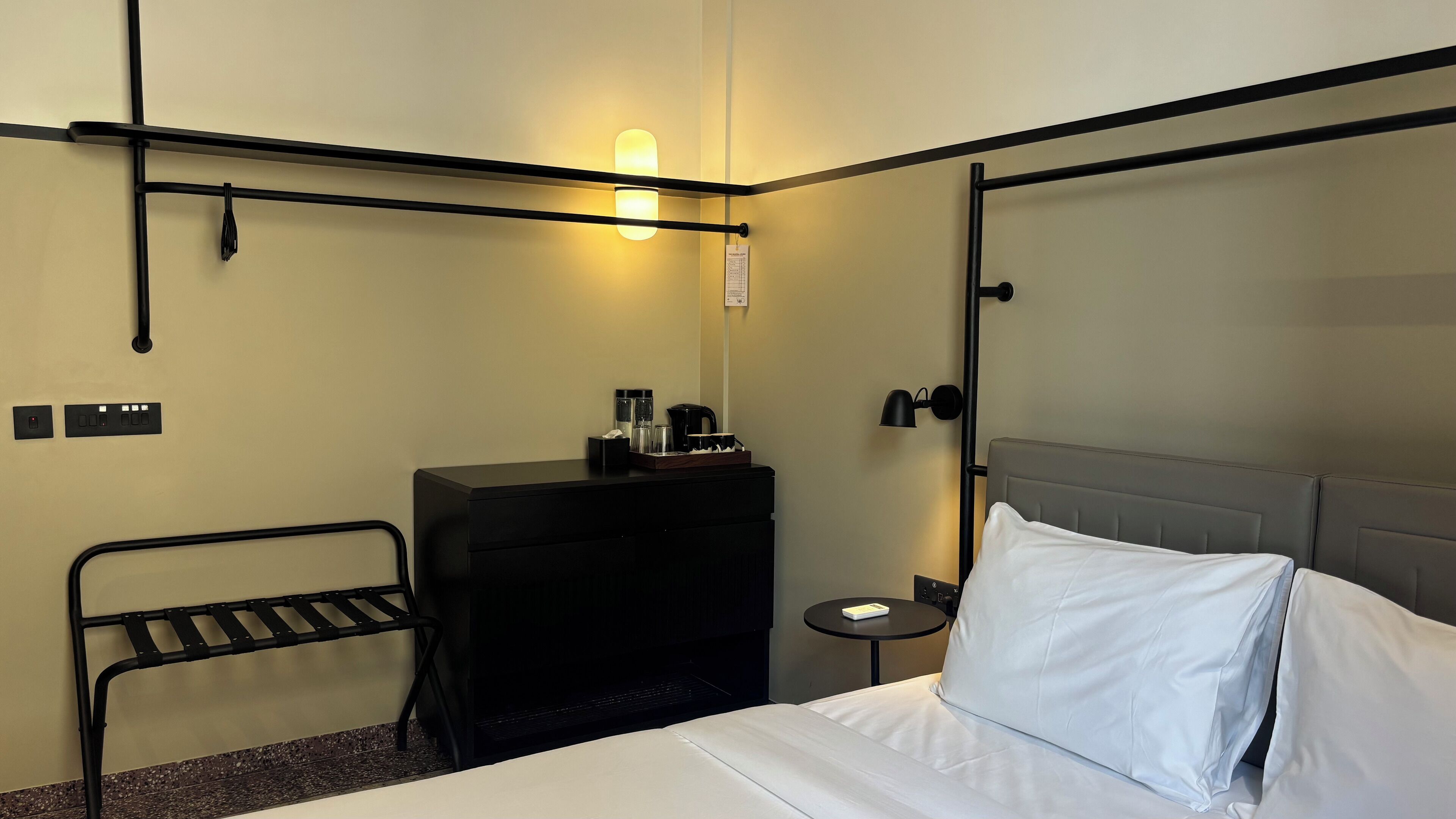 Una habitación de hotel con cama, escritorio con cafetera, lámpara y una mesita.
