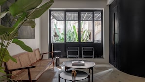 A modern living room with a large window, a sofa, two chairs, a round table, and a potted plant. - Wellesley Hotel (Pune)
