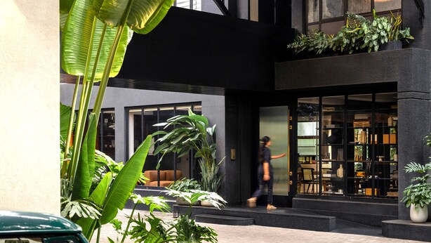 A green vintage car parked in a courtyard with large banana leaves and potted plants. - Wellesley Hotel (Pune)