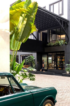 A green vintage car parked in a courtyard with large banana leaves and potted plants. - Wellesley Hotel (Pune)