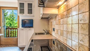 Una cocina moderna con estufa integrada, televisor y un amplio ventanal con vistas a zonas verdes.