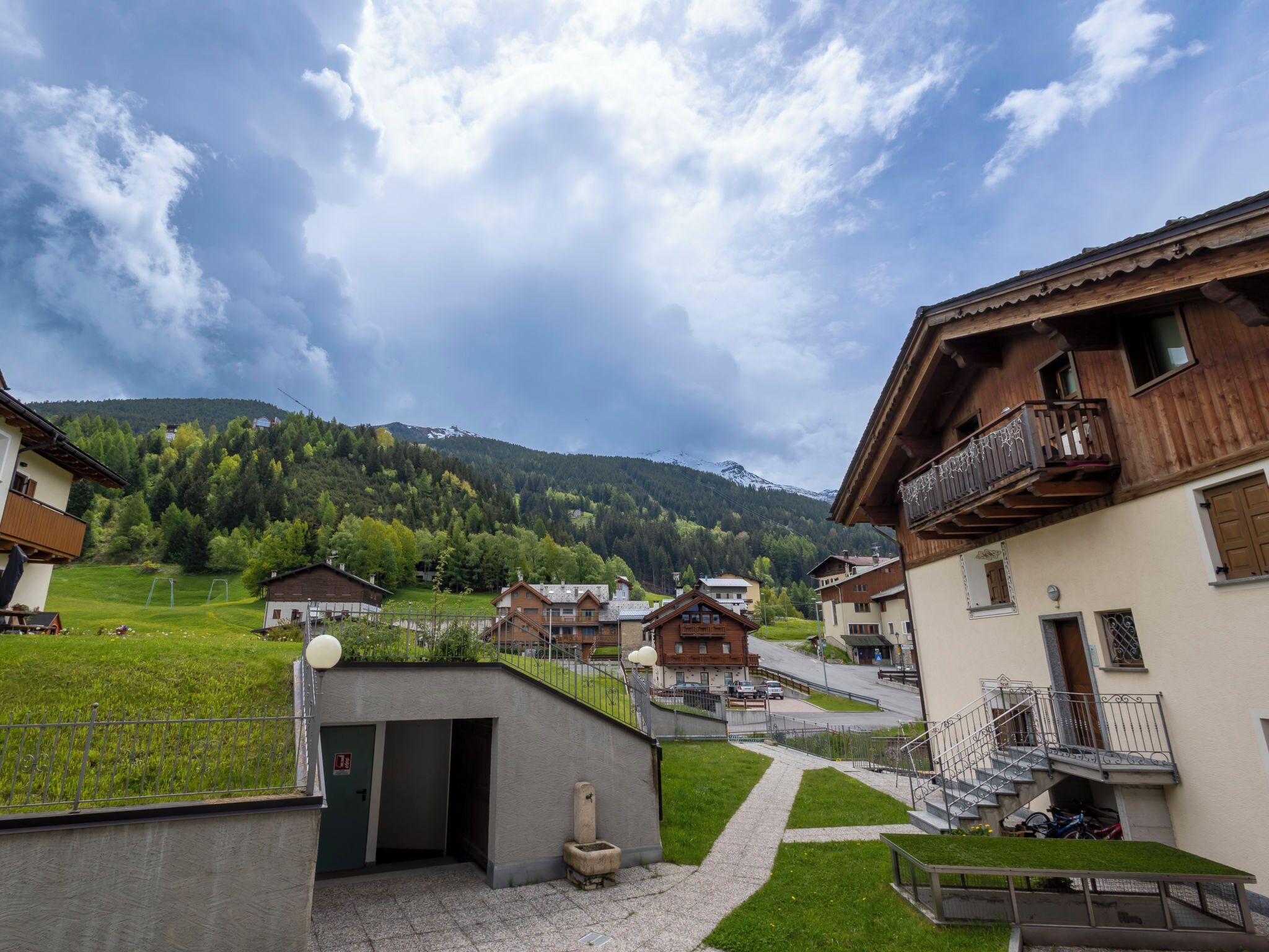A village with traditional wooden houses, a paved path, and a view of a mountain range.