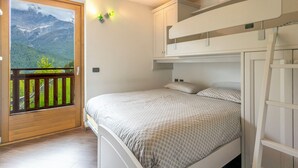 Un dormitorio con una cama, una puerta de madera que da a un balcón y vistas a montañas.