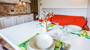 Una cocina moderna con armarios blancos, salpicadero de azulejos y un comedor con una mesa blanca para cuatro personas.