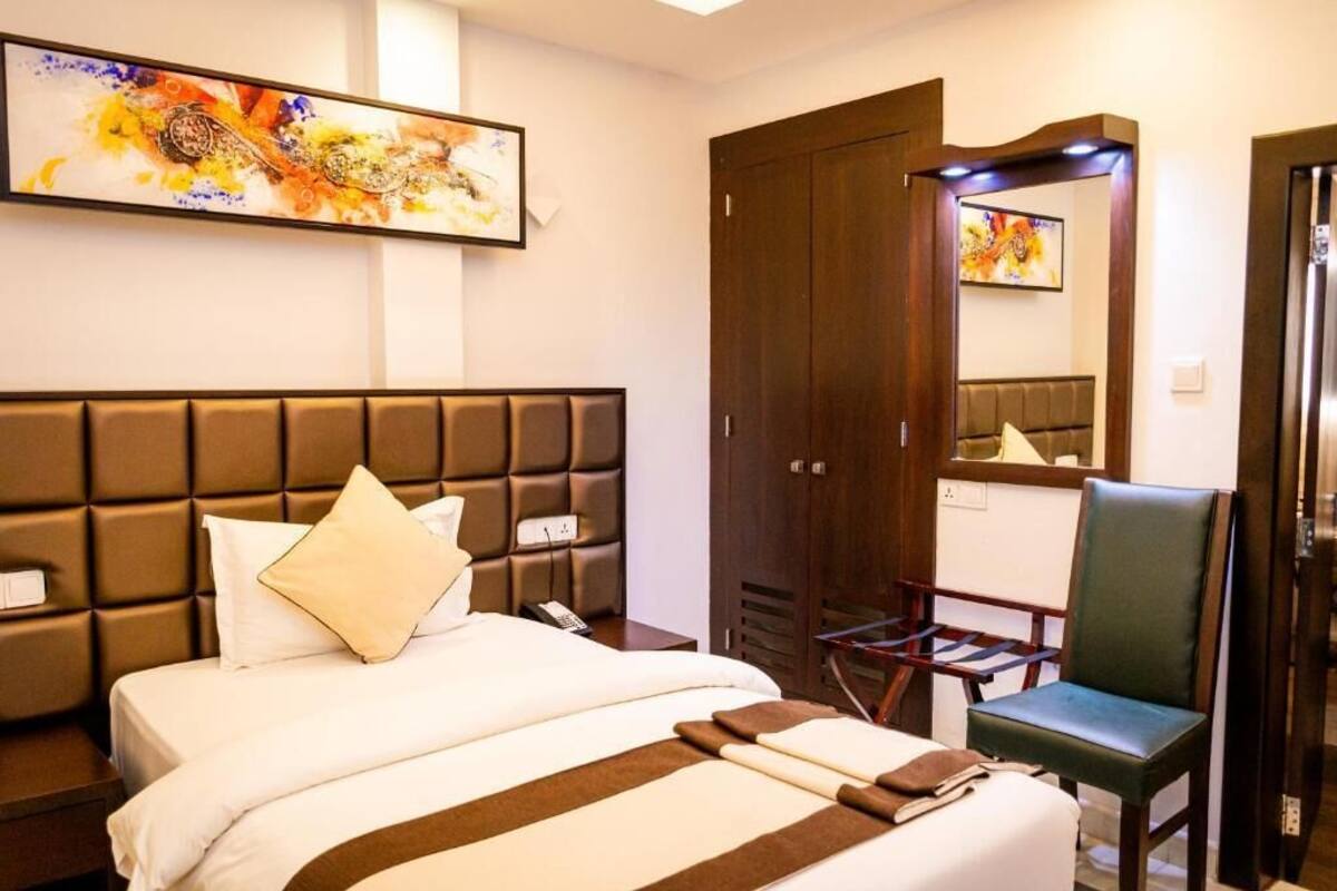 A hotel room with a large bed, a wooden wardrobe, a chair, and a painting on the wall.