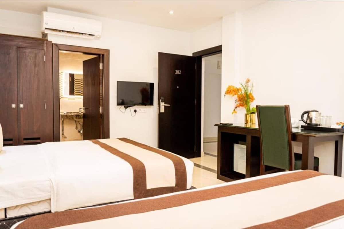 A hotel room with a bed, a desk with a chair, a TV, and a door labeled 102.