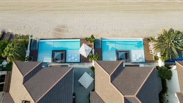Vista aérea de um resort com duas piscinas, uma praia e palmeiras.