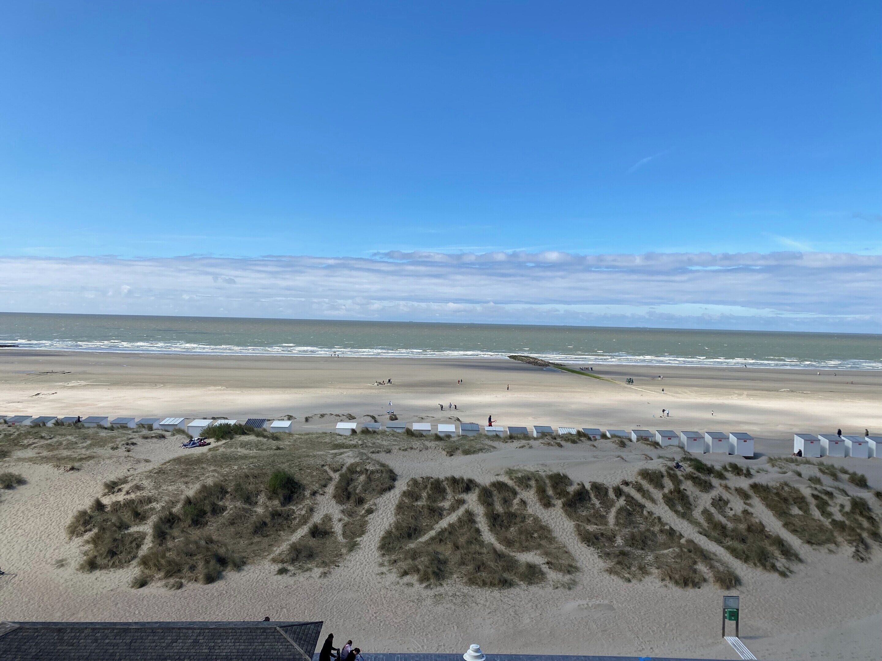 A beach with dunes, a sandy beach, and a clear sky.