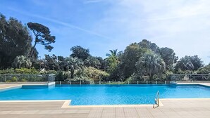 A swimming pool with a wooden deck, surrounded by lush greenery and trees. - Le Grand Parc by Interhome (Saint Aygulf)