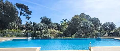 A swimming pool with a wooden deck, surrounded by lush greenery and trees.