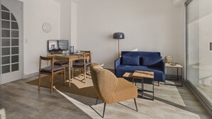 A modern living room with a blue sofa, a wooden dining table, and a brown armchair.