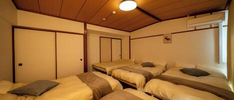 A room with three beds arranged in a row, wooden ceiling, and an air conditioning unit on the wall.