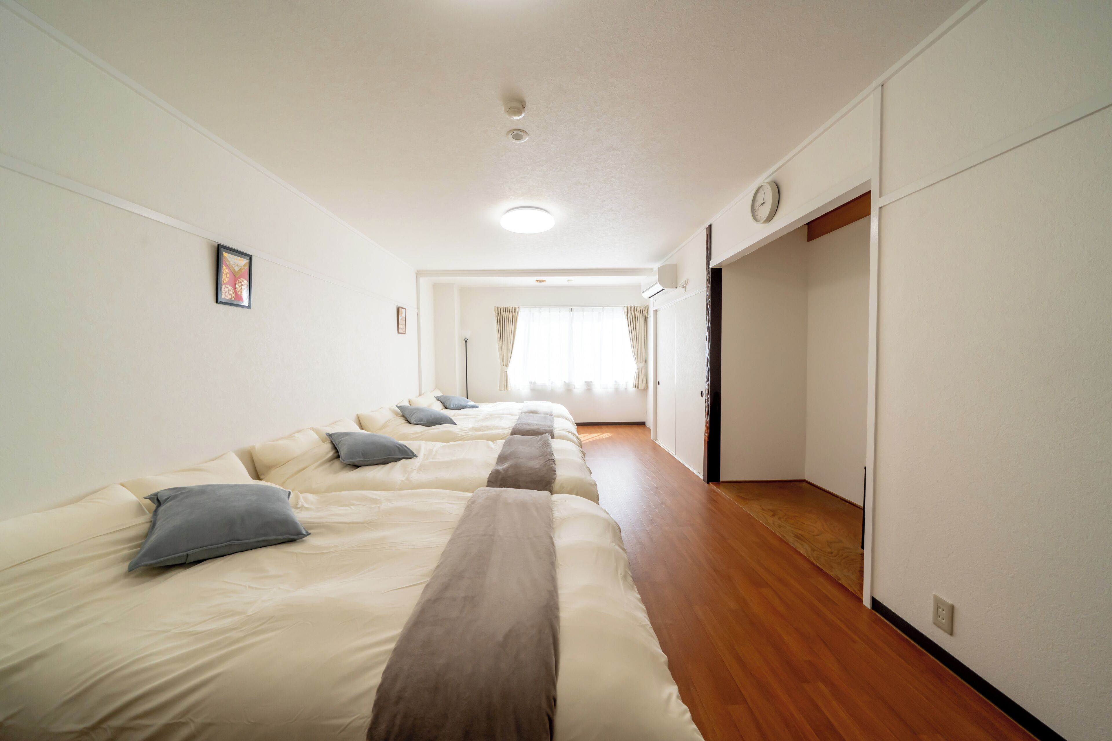 Ein Hotelzimmer mit einem langen Bett, Holzboden und Blick auf den Flur.