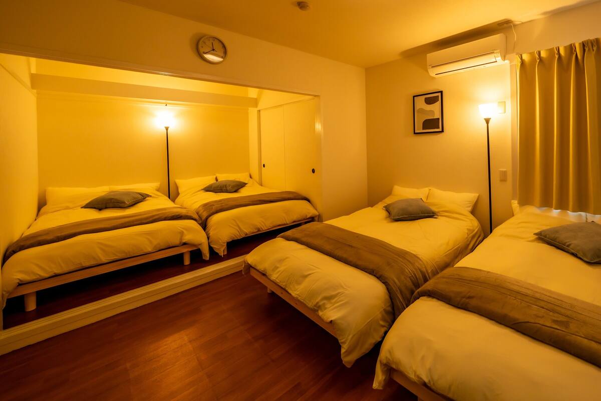 A hotel room with three single beds, a clock on the wall, and an air conditioning unit.