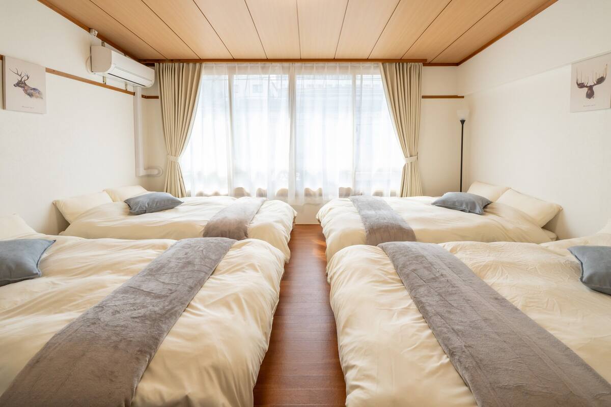 A hotel room with two beds, a wooden ceiling, and a large window with curtains.