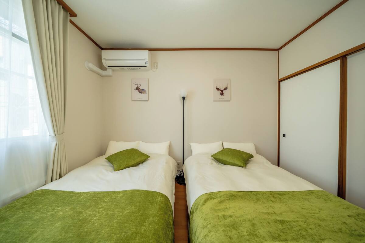 A twin room with two beds, green bedspreads, white pillows, and two deer-themed wall art pieces.