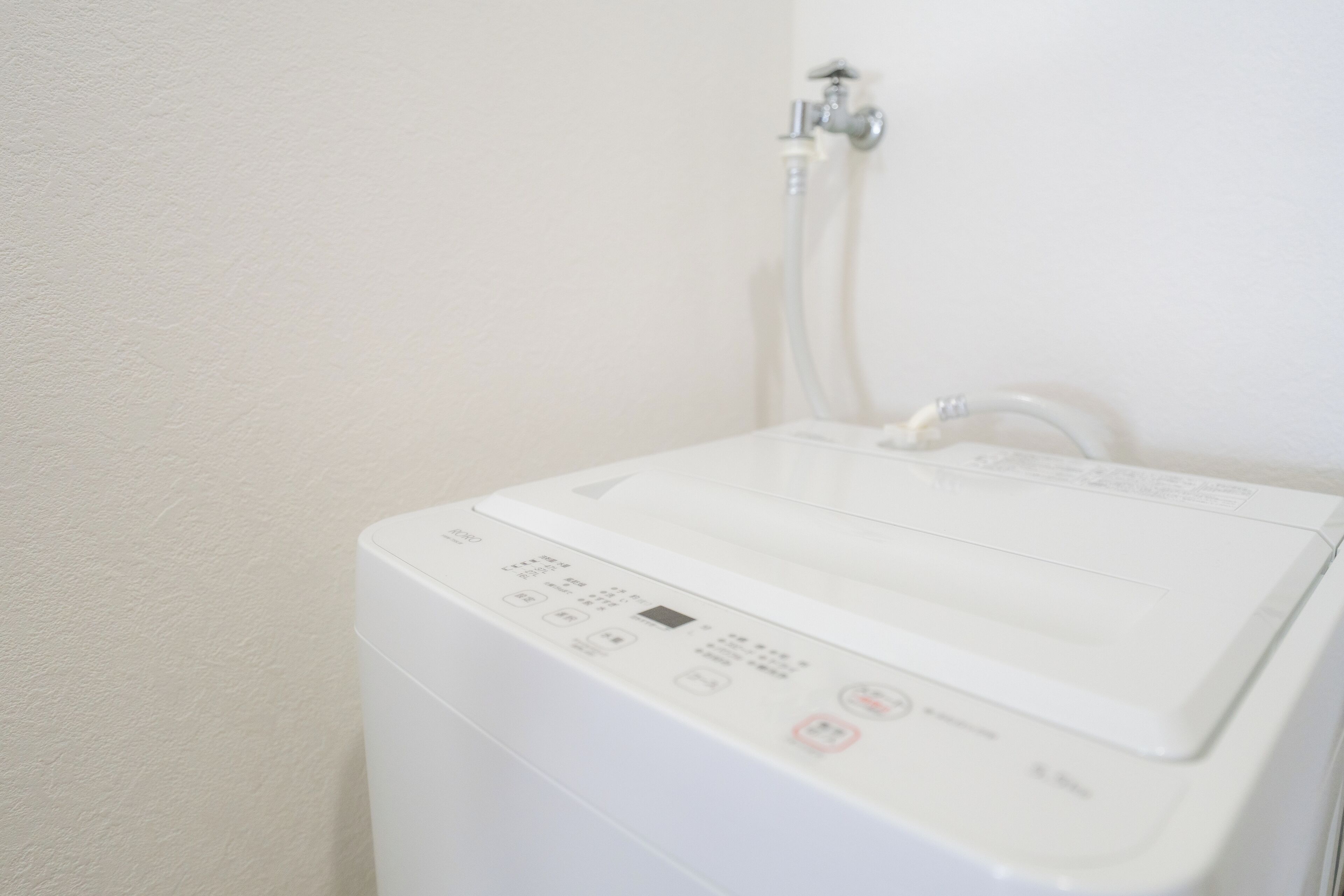 A white washing machine with a control panel and a hose connected to a wall-mounted faucet.