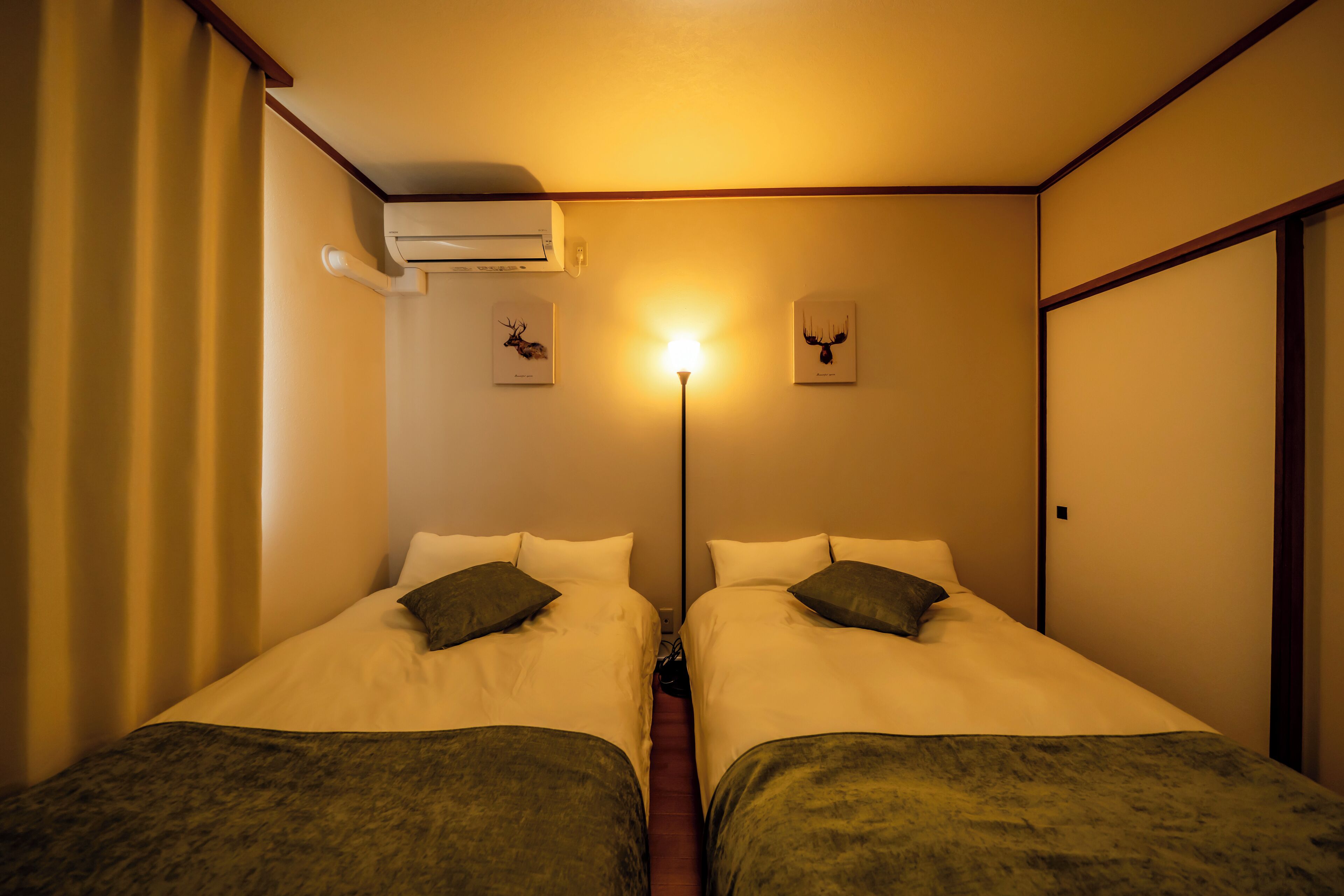 Habitació d'hotel amb dos llits, una làmpada de peu i un aparell d'aire condicionat.