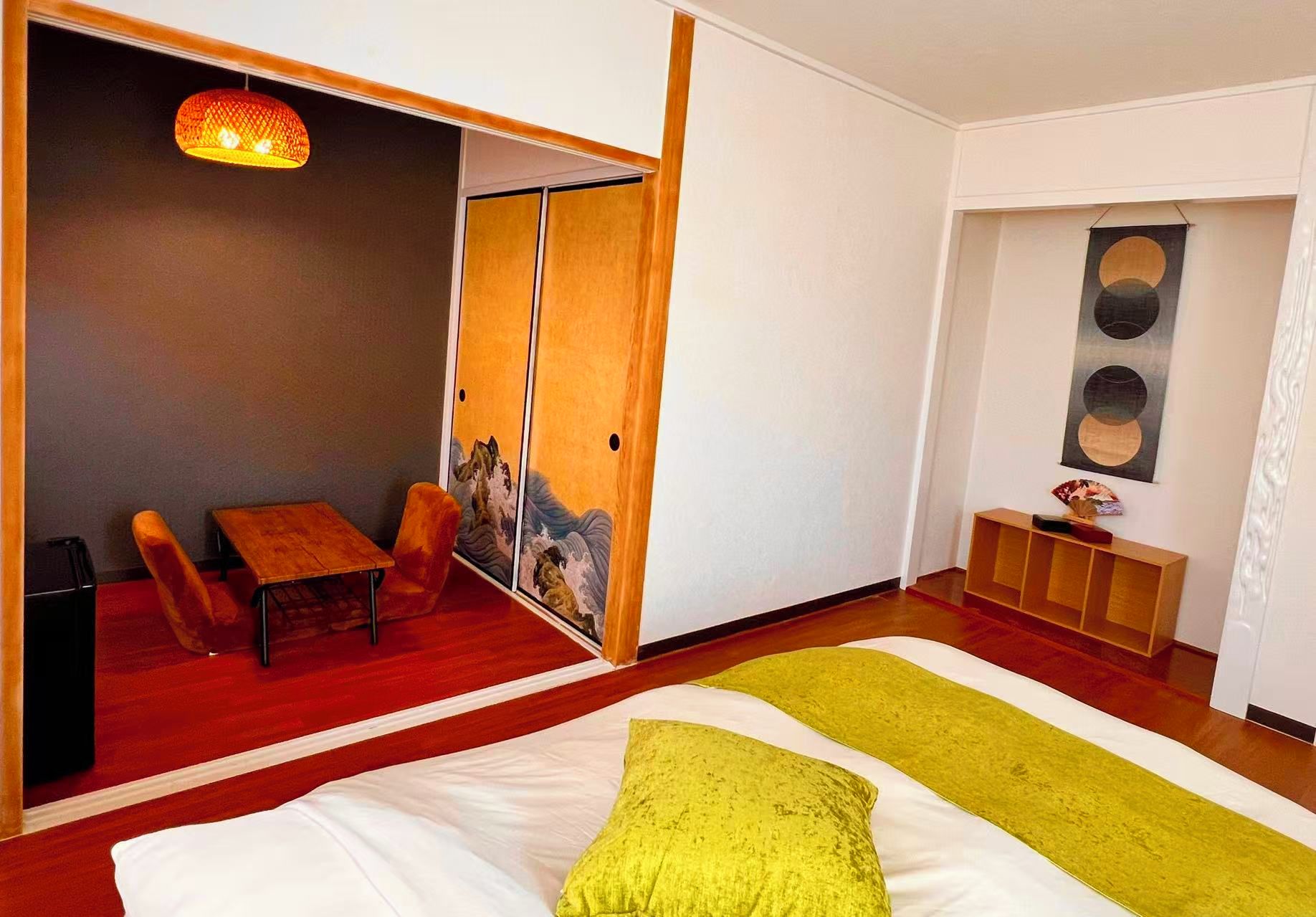 A modern hotel room with a bed, a seating area with a table and chairs, a wall-mounted artwork, and a console table with decorative items.