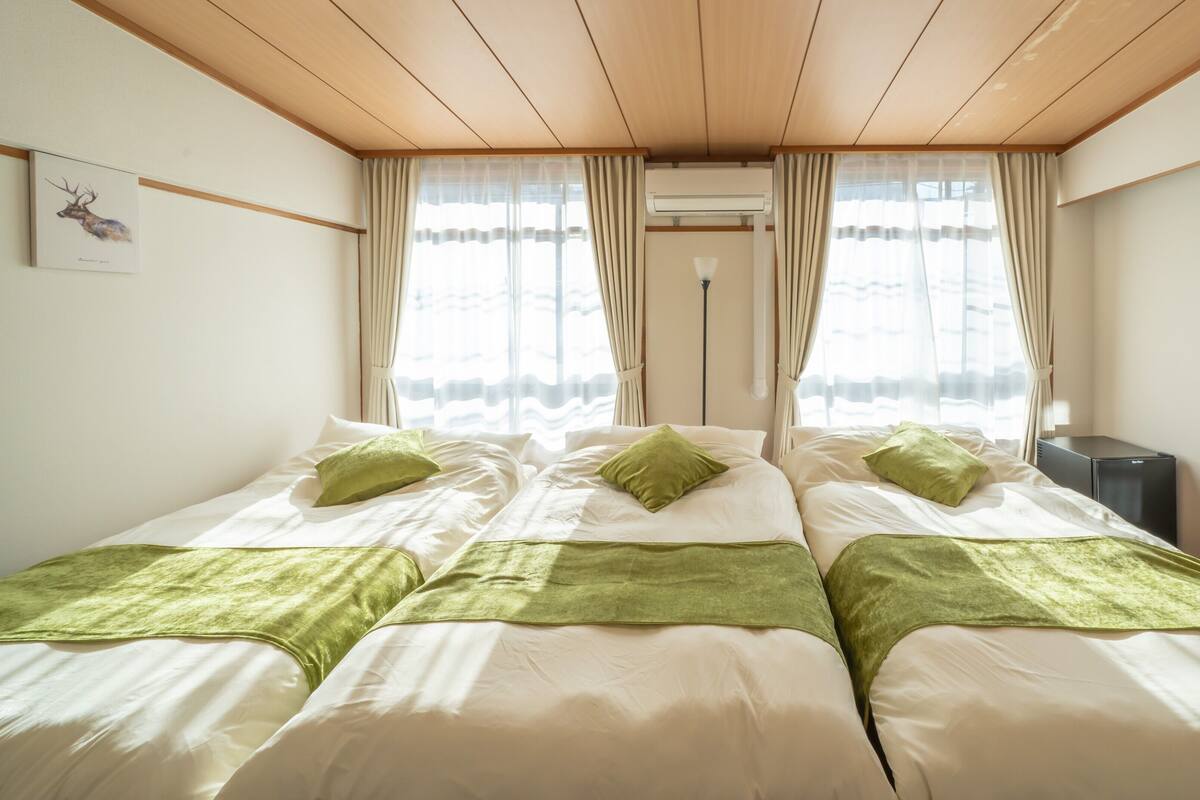 A bedroom with two beds, a window with curtains, an air conditioning unit, and a small bedside table.