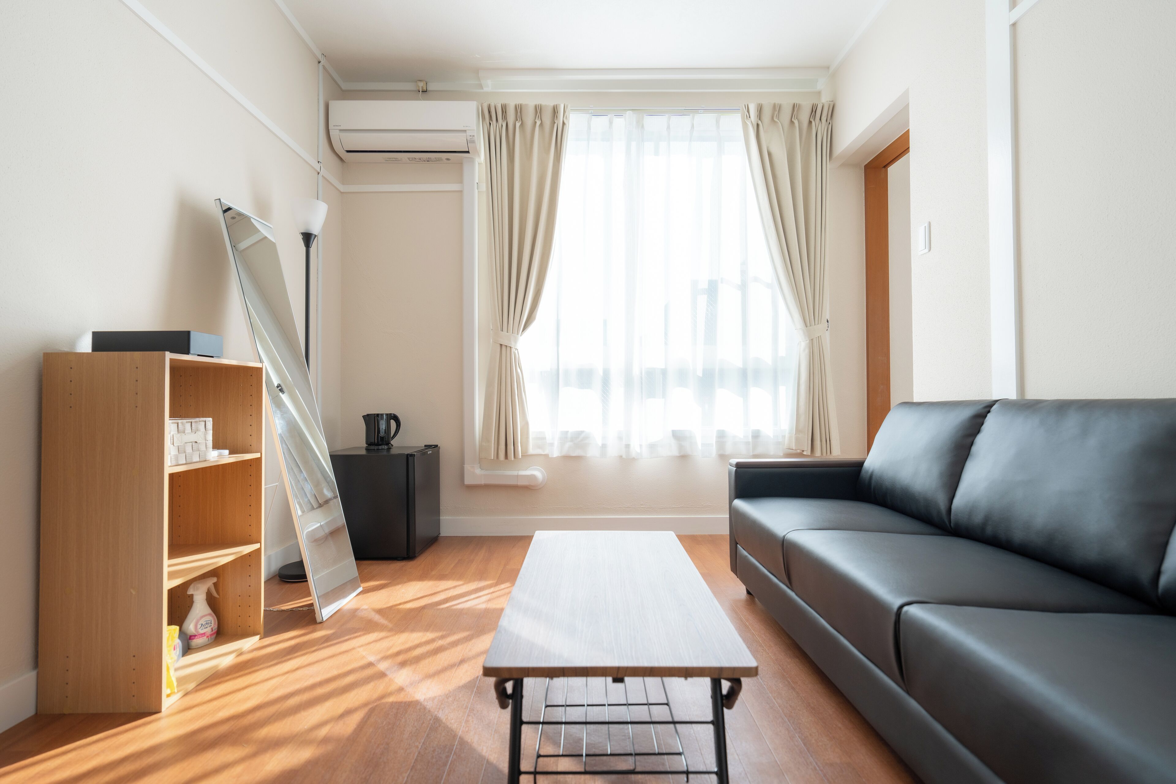 A modern living room with a wooden floor, a black leather sofa, a wooden cabinet, and a small table.