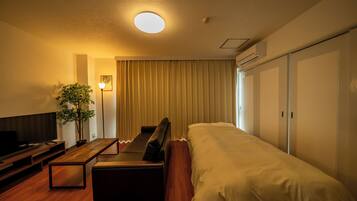 A hotel room with a bed, a sofa, a TV, a plant, and a ceiling light.