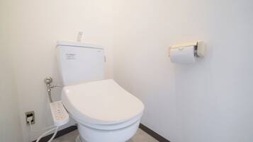 A white toilet with a control panel, a toilet paper holder on the wall, and a visible electrical outlet.