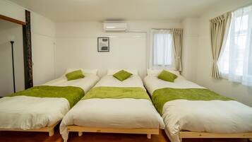 Una stanza con tre letti singoli, ognuno con biancheria da letto bianca e cuscini decorativi verdi. C'è un condizionatore d'aria a soffitto, una finestra con tende leggere e un quadro appeso al muro.