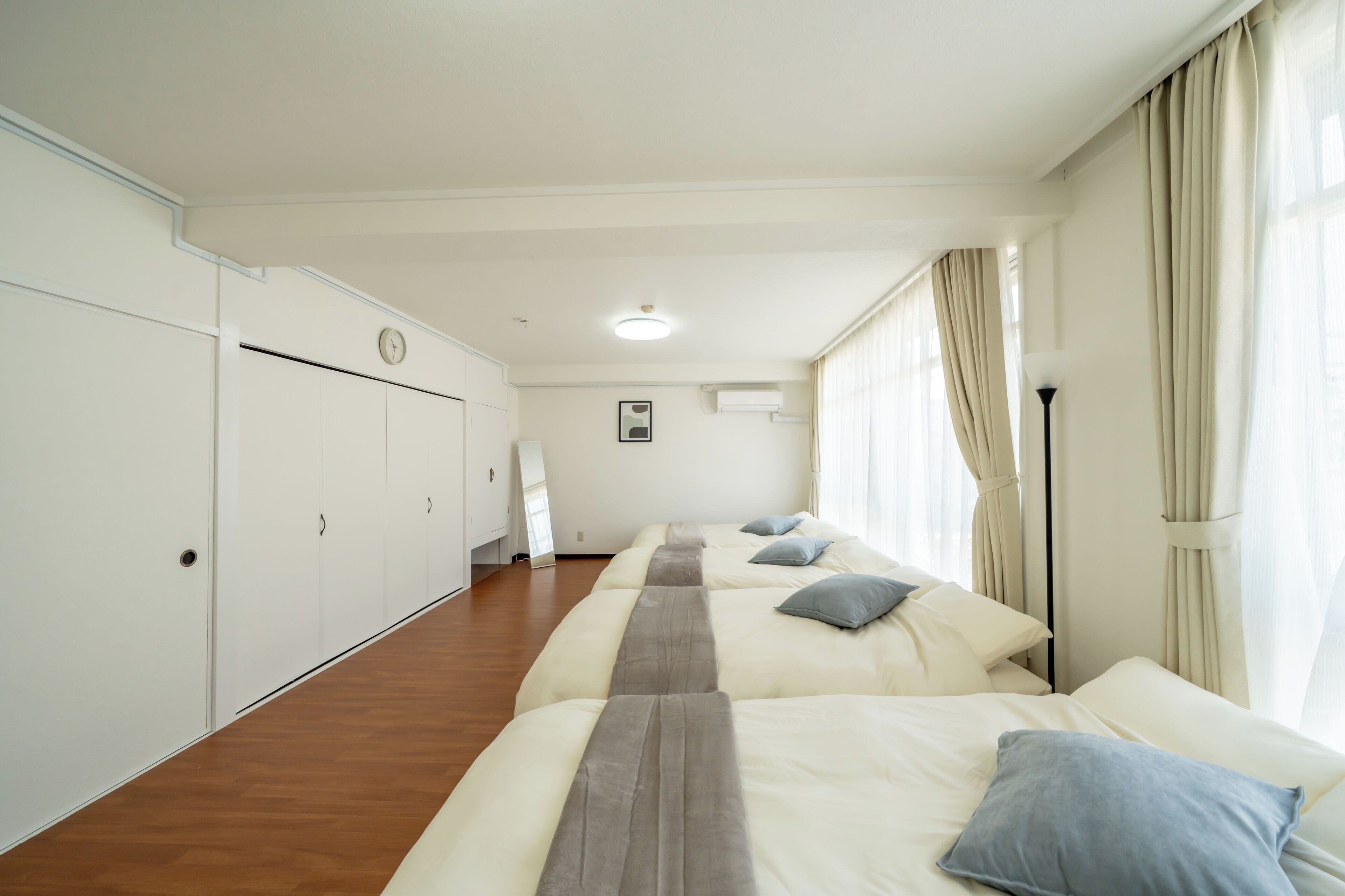 Ett hotellrum med två sängar, trägolv, en väckarklocka på väggen och ett fönster med gardiner.